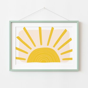 May include: A framed print of a stylised sun with yellow rays and a yellow and white circle in the centre. The background is a light pink colour.
