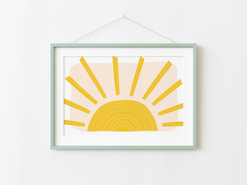 May include: A framed print of a stylised sun with yellow rays and a yellow and white circle in the centre. The background is a light pink colour.