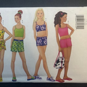 May include: A sewing pattern for girls' swimwear. The pattern includes four different styles of swimwear: a halter top with a wrap skirt, a tank top with shorts, a halter top with shorts, and a tank top with shorts. The pattern is for sizes 7-10.