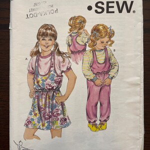 May include: A sewing pattern for a girl's dress and dungarees. The pattern is called "Kwik Sew" and the pattern number is 1551. The pattern is for sizes 8-10, 12-14. The dress is a floral print and the dungarees are pink.