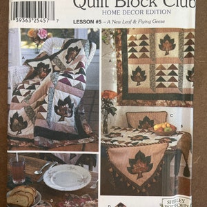 May include: Simplicity Quilt Block Club Home Decor Edition Lesson #5 - A New Leaf & Flying Geese sewing pattern featuring a quilt block design with a leaf motif in shades of brown, green, and pink. The pattern includes instructions for making a throw pillow, table runner, and placemats.