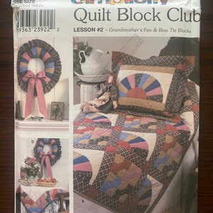 Peut inclure: Un modèle de Quilt Block Club Simplicity, leçon n° 2, présentant les blocs Grandmother's Fan & Bow Tie. Le modèle montre une courtepointe avec une variété de tissus colorés, notamment du rouge, du bleu, du vert et du marron. Le modèle comprend également des instructions pour la réalisation d'une couronne et d'un chemin de table.