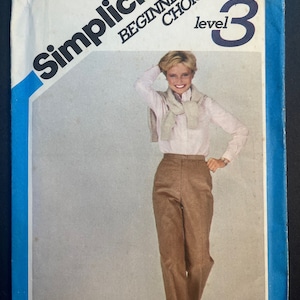 May include: A vintage Simplicity Beginner's Choice sewing pattern, level 3. The pattern features a woman wearing a pink shirt and brown pants. The package includes the size 10, waist 25" measurements. The text "Shirt & sweater not included" is also visible.