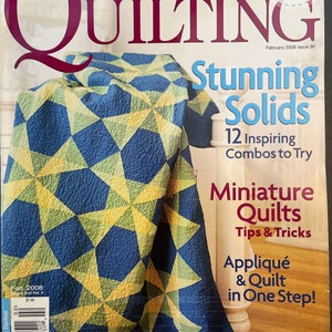 May include: A magazine cover for American Patchwork & Quilting magazine, featuring a quilt made with blue, yellow, and green fabric. The cover text reads "Stunning Solids" and "12 Inspiring Combos to Try".