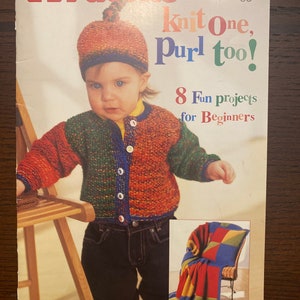 May include: A book cover featuring a colourful illustration of a child wearing a knitted hat and jumper. The book title is "Knit One, Purl Too!" and the subtitle is "8 Fun projects for Beginners". The book cover also includes a small image of a knitted throw.
