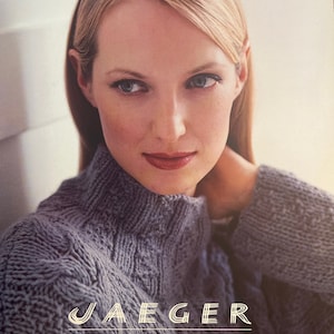 May include: A woman wearing a gray knitted sweater with the text "JAEGER HANDKNITS Ten designer garments using CHAMONIX" on the bottom.