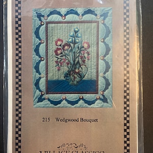 May include: A brown paper pattern for a quilt with a blue and white floral design. The pattern is titled "215 Wedgwood Bouquet" and is from "Village Classics".