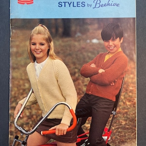 Peut inclure: Une couverture de livre de modèles de tricot vintage représentant deux enfants sur un vélo rouge. Le livre est intitulé "Canadiana Styles by Beehive" et est de Patons, une entreprise de fil. La couverture du livre est jaune, bleue et rouge.