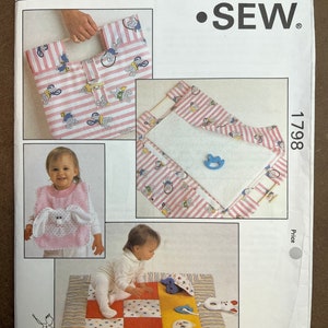 Puede incluir: Un patrón de costura para una alfombra de juego para bebé y un babero. El patrón es de Kwik Sew Pattern Co. Inc. y es el número 1798. La alfombra de juego es de diseño patchwork con un borde de rayas rosa y blanco. El babero es rosa con una aplicación de conejito blanco.