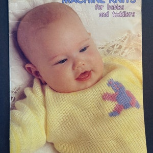 May include: A yellow knitted sweater with a purple and pink bear design for babies and toddlers. The pattern is called "Beehive" and is made with Patons Fairytale DK yarn.