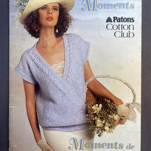 May include: A knitting pattern booklet titled Quiet Moments featuring a light purple short-sleeved wrap sweater with cable knit trim, worn with a straw hat, white skirt, and lace gloves. The cover includes the text Patons Cotton Club.