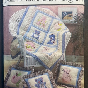 May include: A Simplicity crafts/ouvrages pattern for a baby quilt and pillows. The quilt features a blue and white gingham background with appliquéd teddy bears, flowers, and an apple. The pillows are also blue and white gingham with appliquéd teddy bears, a cat, and an apple.