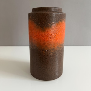Könnte beinhalten: Eine braune und orangefarbene Keramikvase mit strukturierter Oberfläche. Die Vase hat eine breite Öffnung und eine zylindrische Form.