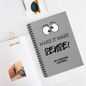 Peut inclure: Un carnet à spirales gris avec le texte "MAKE IT MAKE SENSE!" et "MY VENTING JOURNAL" en noir. La couverture présente un visage de dessin animé avec de grands yeux écarquillés.