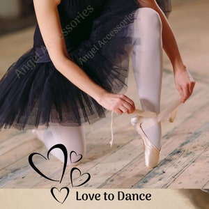 Puede incluir: Una bailarina con un tut&uacute; negro est&aacute; atando la cinta de su zapato de ballet rosa. El suelo es de madera y hay tres corazones negros con el texto "Love to Dance" debajo.