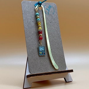 May include: Gold bookmark with a blue and green game controller charm and a beaded chain with red, yellow, and blue beads.