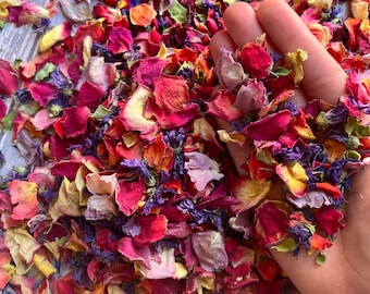 Puede incluir: Una mezcla de pétalos de rosa secos y flores de lavanda en tonos de rosa, rojo, morado y amarillo. Los pétalos están esparcidos sobre una superficie de madera.