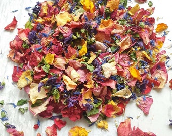 May include: A mix of dried flower petals in shades of red, orange, yellow, and blue. The petals are scattered on a white surface.