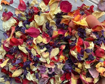 May include: A mix of dried flower petals in shades of red, pink, yellow, and purple. The petals are scattered on a wooden surface.
