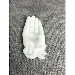 May include: A white, hand-shaped decorative object with a floral design at the wrist. The hand is in an open position, with fingers extended. The floral design includes a flower and leaves. The object is made of a translucent material.