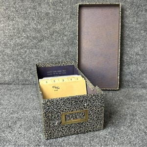 May include: An open agate card index tray with a black and white speckled pattern. The tray contains numbered index cards and a brass label holder. The lid is open and the interior is purple.