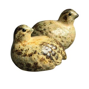 May include: Two small ceramic bird figurines with a speckled cream and brown finish. Each bird features a rounded body, a short pointed beak, and a small black eye, with dark brown mottled markings across the surface of the glaze.