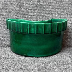 May include: A vibrant green ceramic planter with a textured, ridged rim. The cylindrical pot has a glossy finish, showcasing the rich emerald hue. This decorative piece is suitable for indoor or outdoor use.
