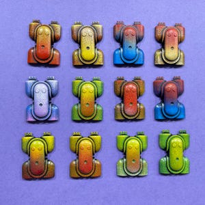 May include: A grid of twelve colourful, abstract, robot-like sculptures on a purple background. Each sculpture features a unique colour gradient, including red, yellow, blue, and green. The sculptures have a textured, metallic appearance.