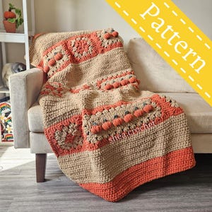Puede incluir: Una manta de punto de crochet con temática de calabaza. La manta está hecha en un esquema de color beige y naranja con un patrón texturizado. La manta está colocada sobre un sofá.