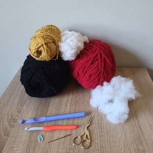 Puede incluir: Una colecci&oacute;n de hilo en colores negro, rojo, blanco y amarillo, junto con relleno, un gancho de ganchillo, tijeras y un marcador de punto.