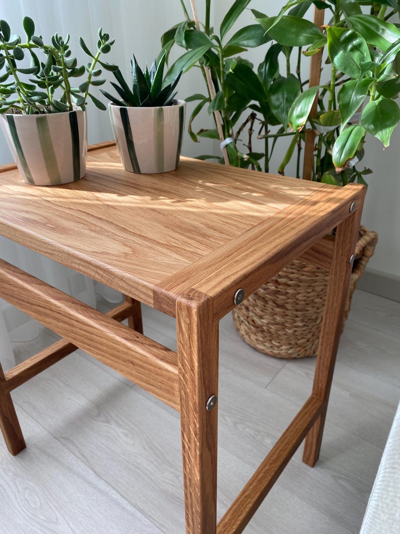 May include: A rectangular side table constructed from light brown wood with a visible grain pattern. The table features four straight legs connected by horizontal support bars and is assembled with visible silver-toned metal circular fasteners.