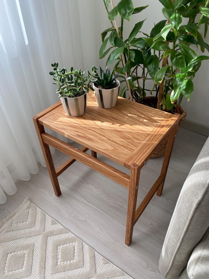 May include: A small, wooden side table with a natural finish. Two potted succulents sit on the table's surface. The table has a rectangular top and angled legs. The table is approximately 24 inches tall and 18 inches wide.