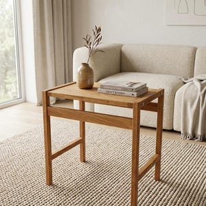 May include: A rectangular wooden side table with four straight legs and a horizontal support bar. On the tabletop sits a tan ceramic vase containing a single dried branch and two stacked books titled Japandi Home and Craft & Form.