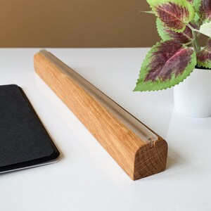 May include: A wooden display stand with a clear acrylic strip running along the top. The stand is made of natural wood with a light brown color. The stand is perfect for displaying small items, such as jewelry, cards, or photos.