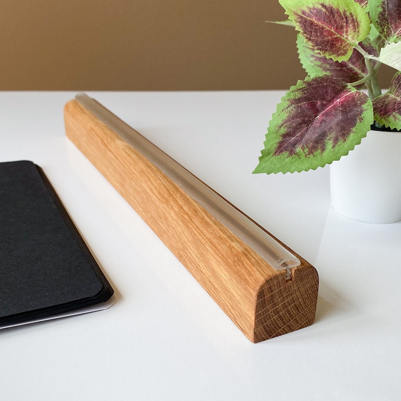 May include: A wooden display stand with a clear acrylic strip running along the top. The stand is made of natural wood with a light brown color. The stand is perfect for displaying small items, such as jewelry, cards, or photos.