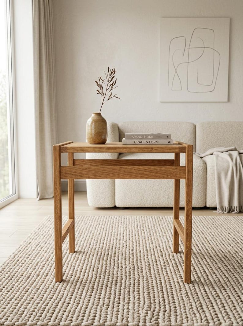 May include: A light brown wooden console table with a rectangular top and four straight legs. On the table surface sits a tan ceramic vase containing a single dried branch and two stacked books titled Japandi Home and Craft & Form.