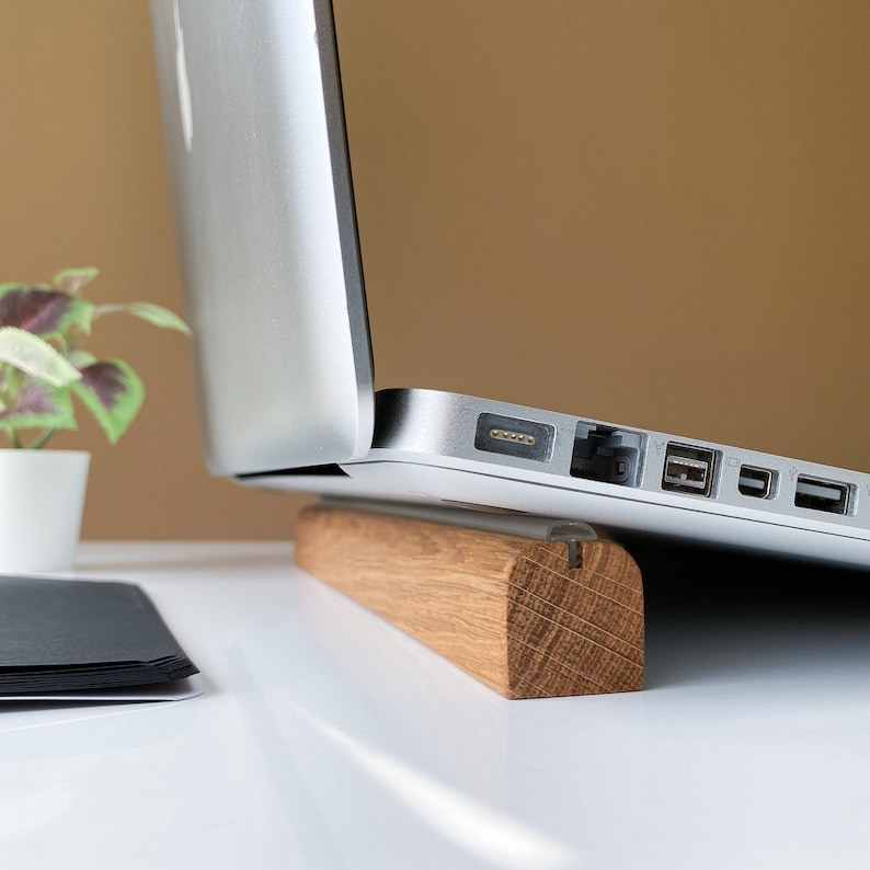 May include: A silver laptop computer is elevated on a wooden stand. The laptop is open and the stand is made of light brown wood.