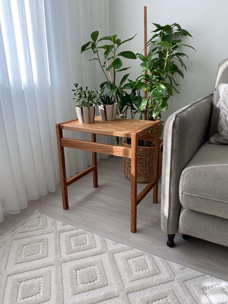 May include: A rectangular wooden side table with four straight legs and a flat top surface. The table is constructed from light brown wood with a visible grain pattern and features a simple frame design with horizontal support bars on the sides.