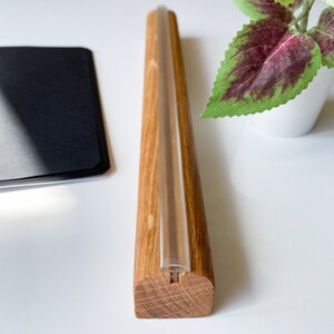 May include: A wooden stand with a clear glass tube running through it. The stand is made of light brown wood and has a natural finish.