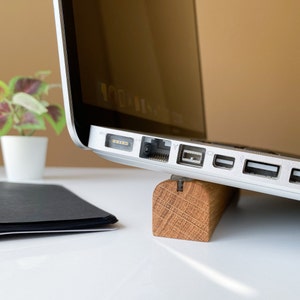 May include: A silver laptop computer with multiple ports on the side is resting on a wooden stand. The laptop is on a white surface.