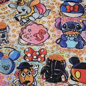 May include: A colorful fabric with a variety of Disney characters, including Mickey Mouse, Stitch, Darth Vader, and Dumbo. The fabric is covered in a pattern of small yellow circles.