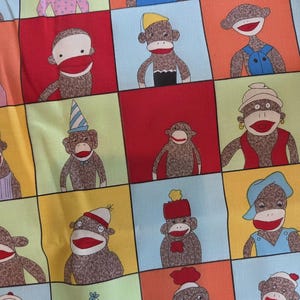 May include: A fabric pattern featuring a grid of colorful squares, each containing a brown sock monkey illustration. The monkeys are depicted with red mouths, white faces, and various accessories including hats, vests, and necklaces in diverse colors.