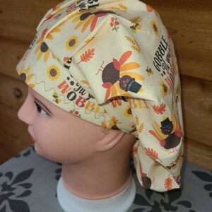 May include: A yellow and orange patterned scrub hat with a turkey design and the text "Gobble 'til you wobble".