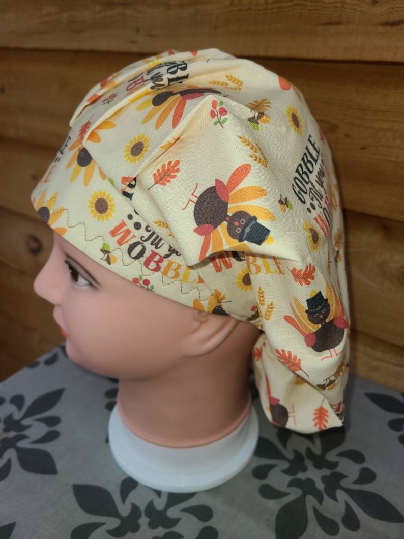 May include: A yellow and orange patterned scrub hat with a turkey design and the text "Gobble 'til you wobble".
