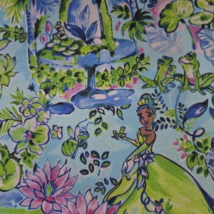 May include: A light blue fabric featuring a repeating pattern of a character in a green gown, frogs, a flying insect, and pink lotus flowers. The design includes a blue fountain, green foliage, and various aquatic plants in shades of green and pink.