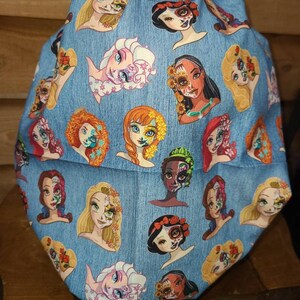 May include: A blue fabric with a pattern of various Disney princesses with sugar skull makeup. The princesses include Elsa, Anna, Belle, Ariel, Snow White, and Rapunzel.