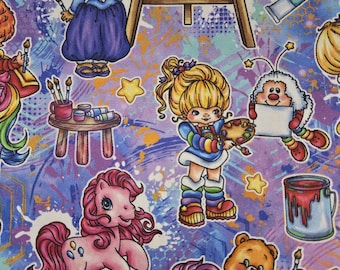 May include: A fabric print featuring a purple background with colorful splatters and stars. The pattern includes cartoon characters, a wooden easel, paint tubes, a small table with brushes, a pink pony, and a paint can with red paint.