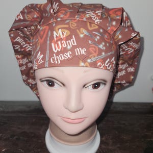 May include: Brown scrub hat with a white and gold print of wands and the text "My Wand Chose Me".