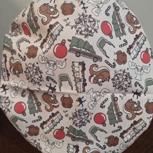 May include: A scrub cap featuring a cream-colored background with a repeating holiday pattern. The print includes brown squirrels wearing Santa hats, roasted turkeys, red ornaments, green Christmas trees on cars, campers, moose, and candy canes.