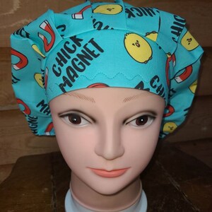 May include: A turquoise blue surgical scrub hat with a white and yellow chick magnet design. The hat has the words "Chick Magnet" printed on it.
